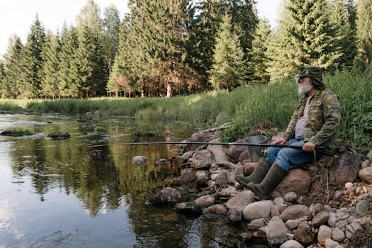 一位长着胡子的老人在树木环绕的平静河边钓鱼