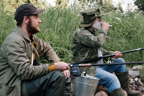 Free Two men fishing and enjoying nature near a lush green lakeside. Stock Photo