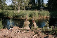 两个男人在宁静的乡村河边，一起坐着钓鱼