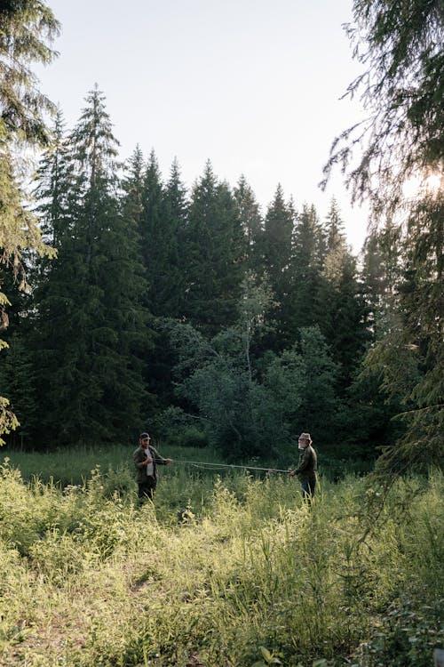 2 Person Walking on Green Grass Field Surrounded by Green Trees