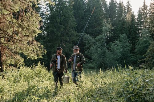 Free Two men with fishing rods walking through a lush forest setting. Stock Photo