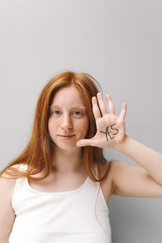 Red-haired woman with a confident expression holding up hand with 'Yes' written, in a minimalist studio setting.