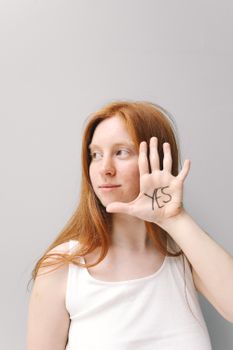 Confident woman shows 'Yes' written on her hand with a grey background.