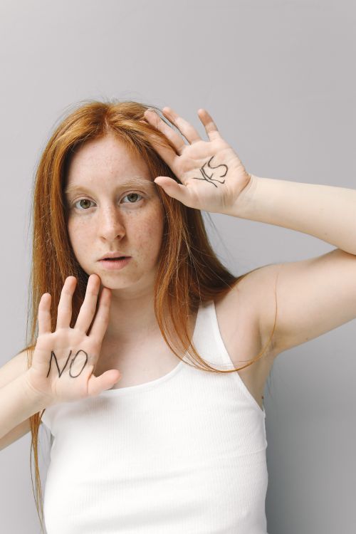 Free A woman with red hair contrasts 'no' and 'yes' with hand gestures in a white tank top. Stock Photo