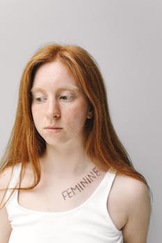 这是一位红发女子的特写肖像，她肩上有雀斑和“女性化”纹身，彰显着身份