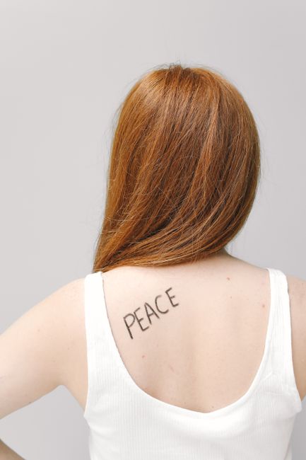 A woman with red hair and a peaceful message tattooed on her back, photographed in a minimalist style.
