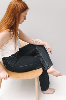 A young woman sitting with 'Be Kind' tattoo on her arm, emphasizing compassion.