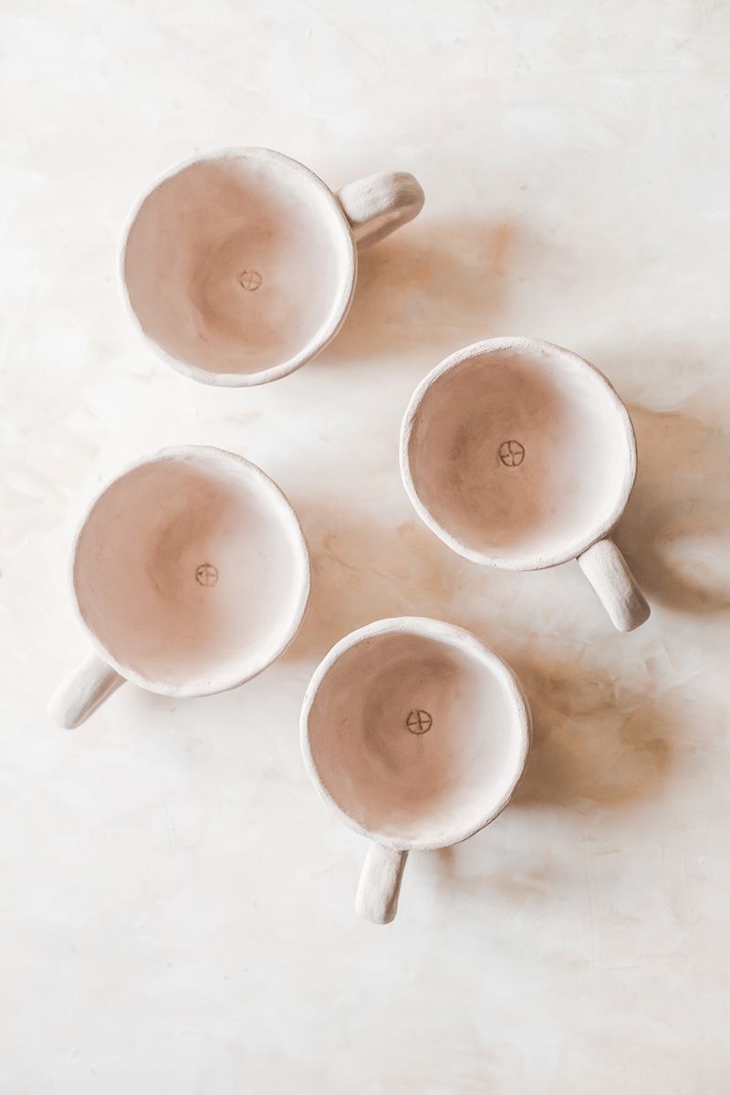 Four matte stoneware mugs in warm sand glaze, arranged on a pale table — photo by Diana Light on Pexels