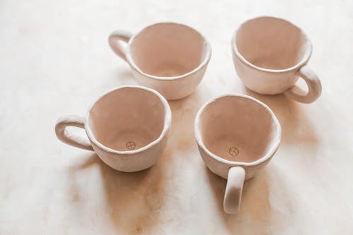 From above of empty craft ceramic cup placed on beige surface in workshop