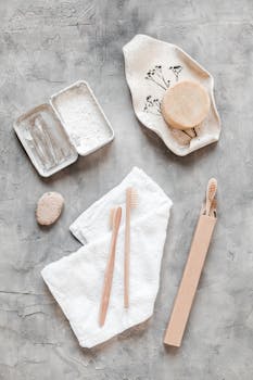 Flat lay of sustainable bathroom products like bamboo toothbrushes, soap, and towels on a marble background.