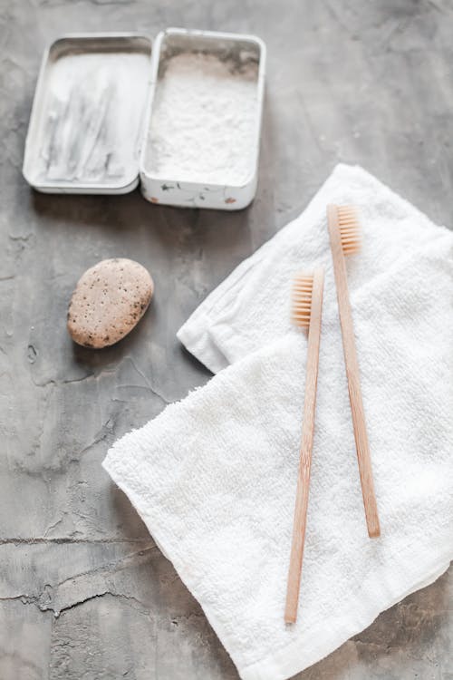 From above eco friendly bamboo toothbrushes and organic toothpaste with white towel placed on gray surface