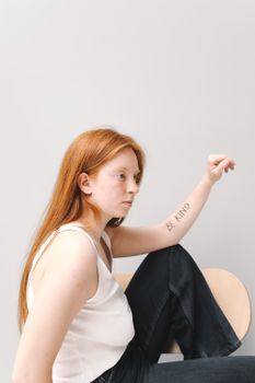 Side view of a woman with 'Be Kind' tattoo on her arm, sitting indoors.