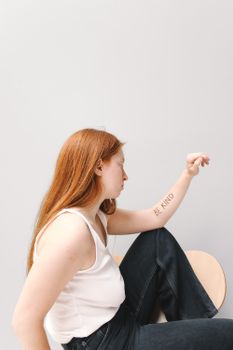 Side view of a young woman with 'Be Kind' text, posing in a studio setting.