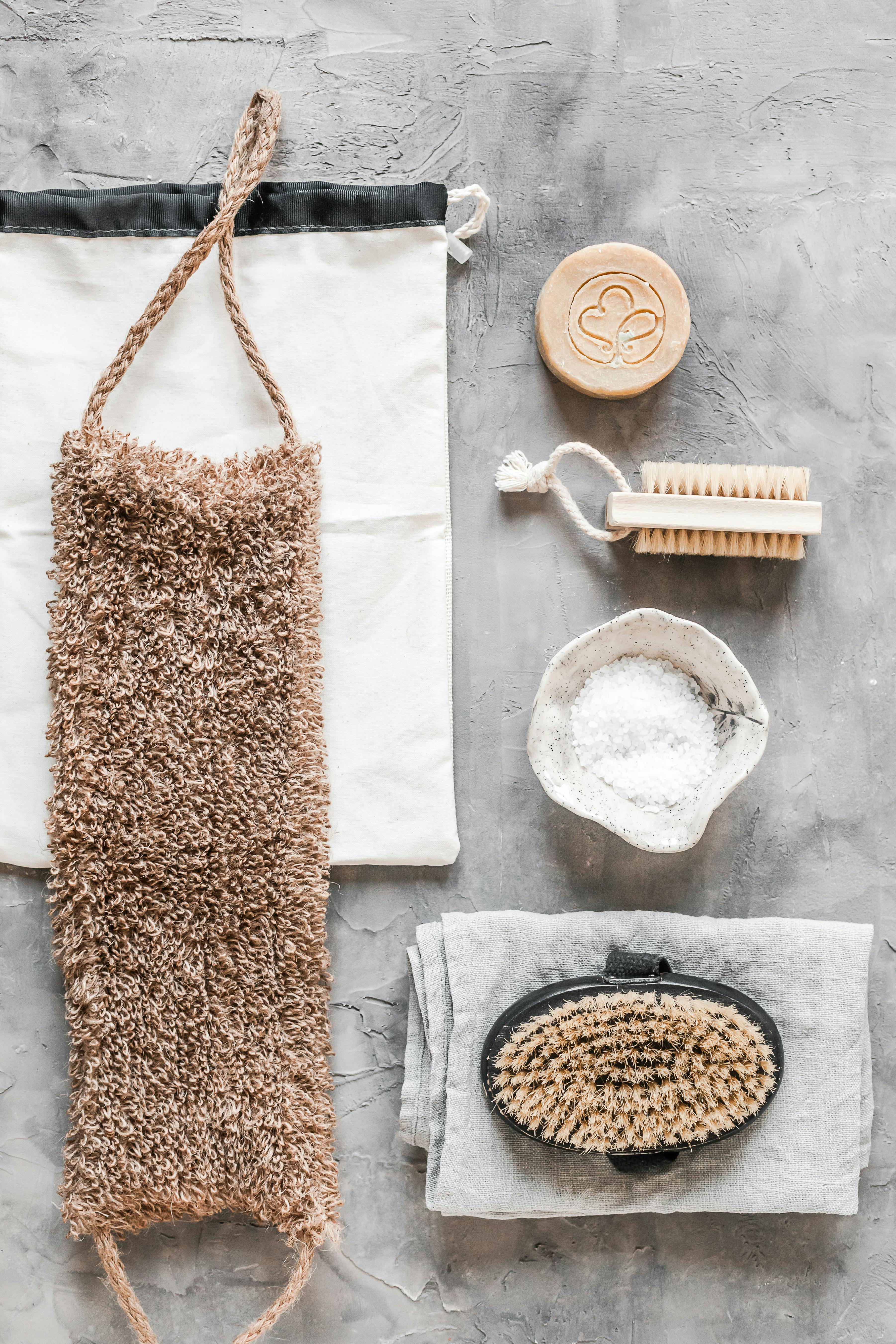 Flat lay of sustainable bath products including natural scrub and soap on a grey background.