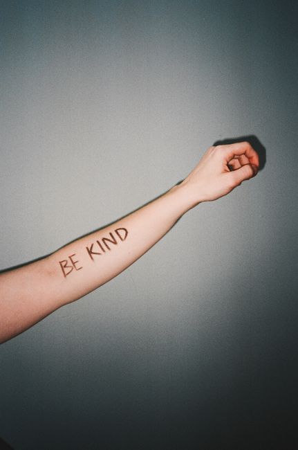 Close-up of a forearm with 'Be Kind' written, symbolizing kindness and positivity.