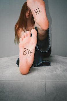 Creative portrait of a woman with 'Hi' and 'Bye' written on her soles, evoking playful communication.