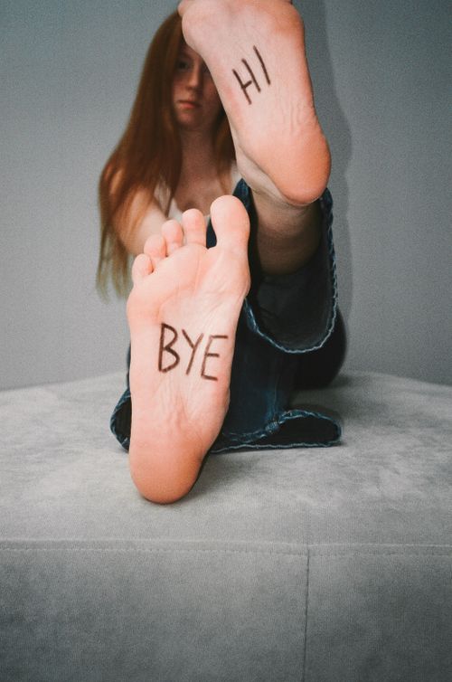 Free Creative portrait of a woman with 'Hi' and 'Bye' written on her soles, evoking playful communication. Stock Photo