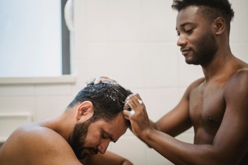 Free An interracial couple shares a tender moment as one washes the other's hair in a shower. Stock Photo