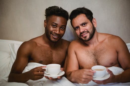 Two men enjoying a relaxed morning with coffee in bed, showcasing love and companionship.
