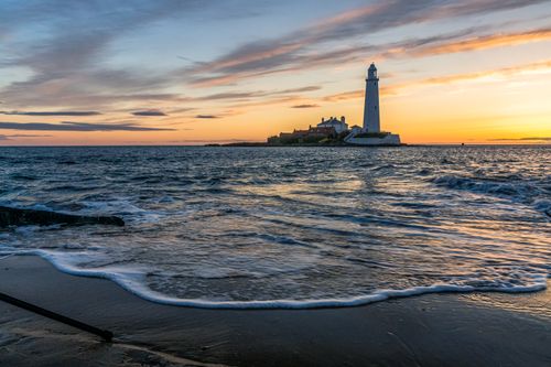 Free Beautiful sunset with a lighthouse on the seacoast, waves lapping gently at the shore. Stock Photo