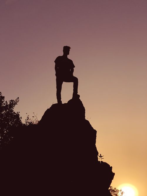 Free Silhouette of a lone hiker on a rocky cliff during a stunning sunset, symbolizing adventure. Stock Photo