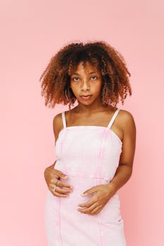 Studio portrait of a young woman with curly hair against a pink background, embodying beauty and confidence.
