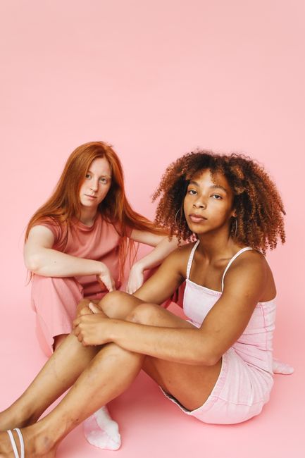 Two young women posing stylishly on a pink background, symbolizing friendship.