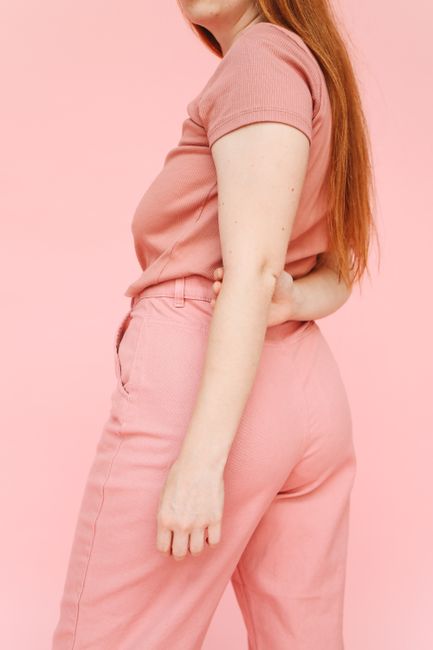 Stylish young woman in pink attire poses against a light pink studio background.