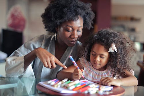 A Woman Teaching a Young Girl Coloring on the Book