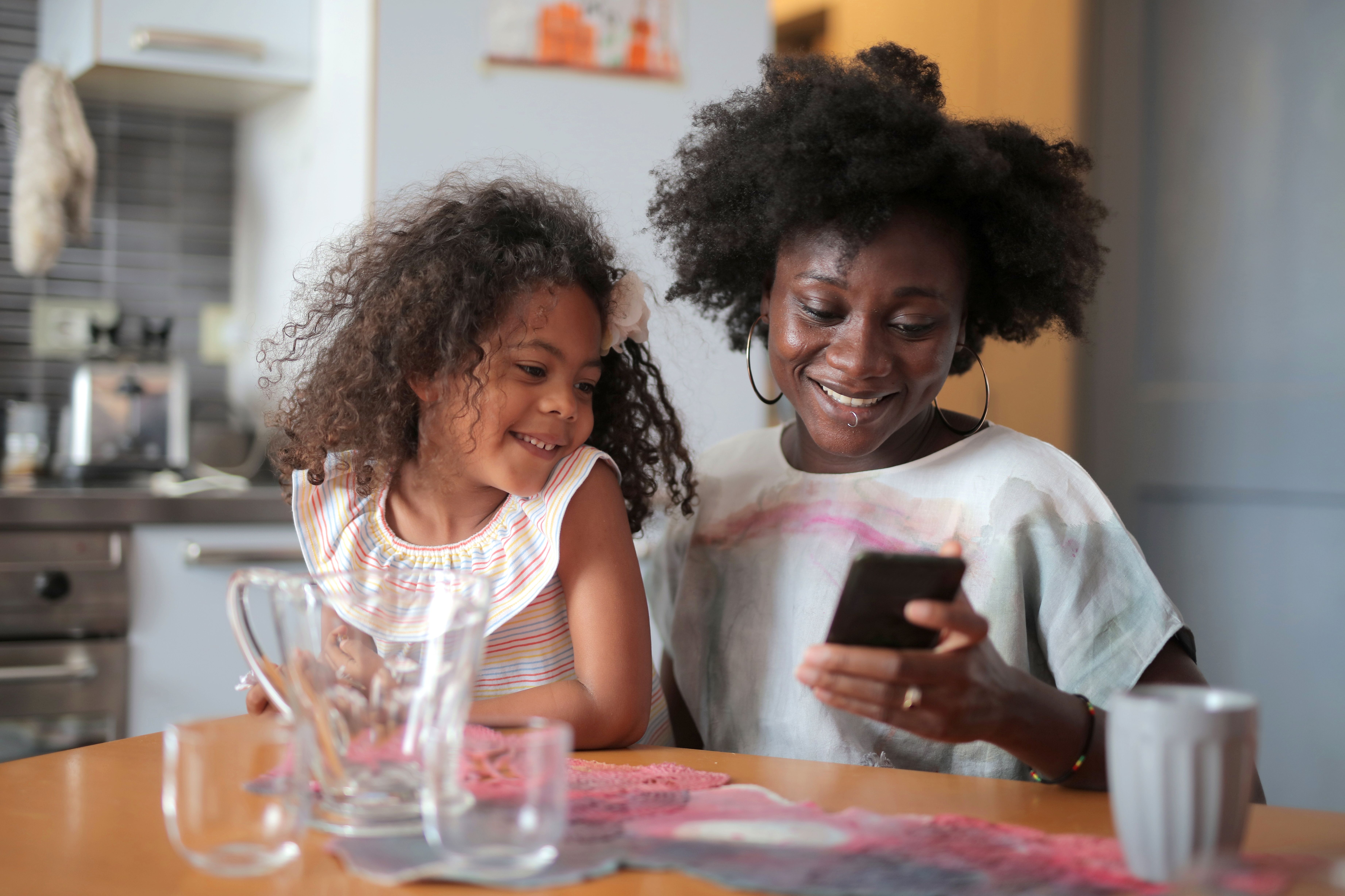 Un moment joyeux entre une mère et sa fille se liant sur un téléphone dans une cuisine.