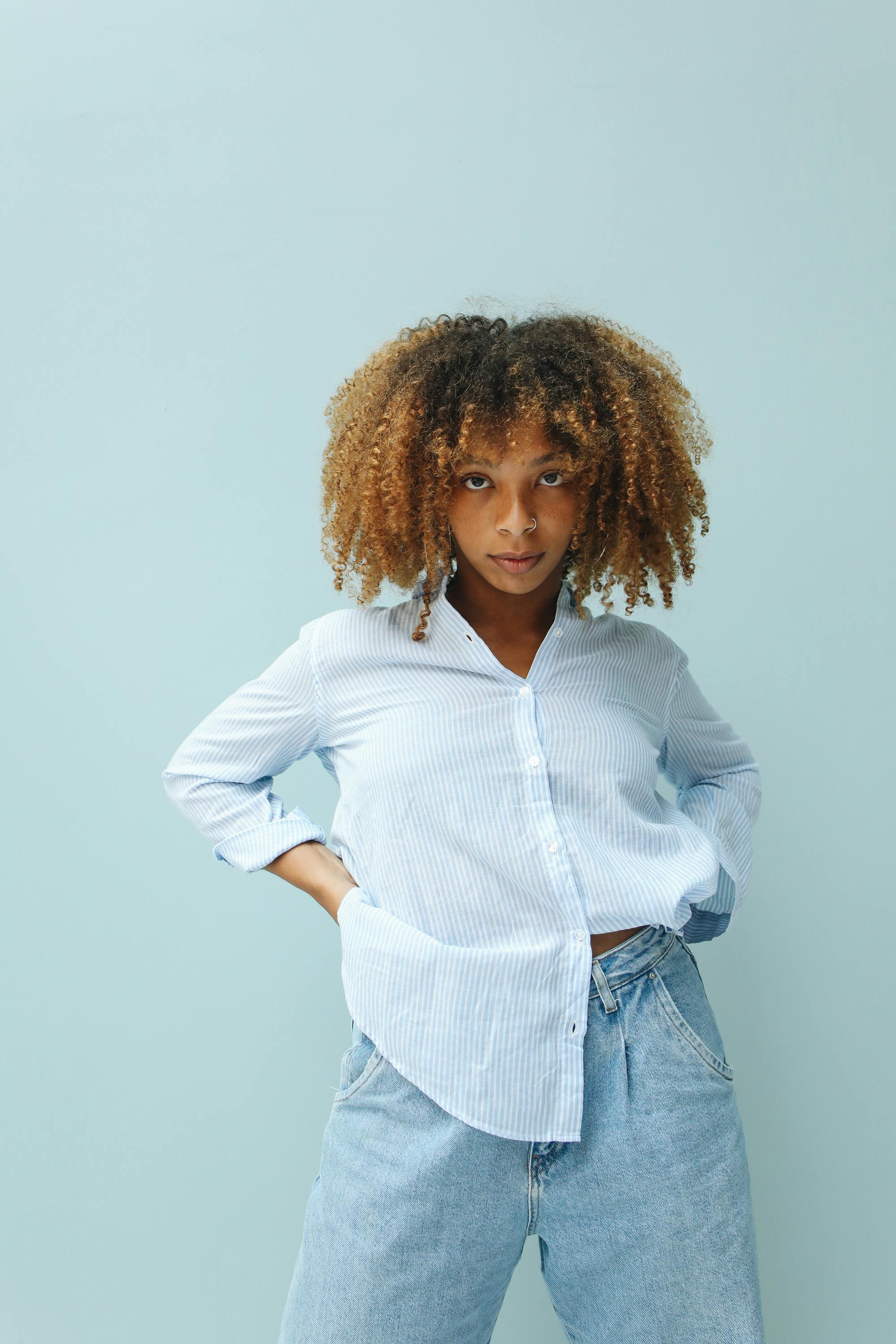 A fashionable black woman with afro hair poses confidently against a light blue background.