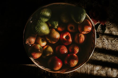 From above of appetizing freshly picked apples arranged with ripe avocados in bowl placed on tablecloth in kitchen