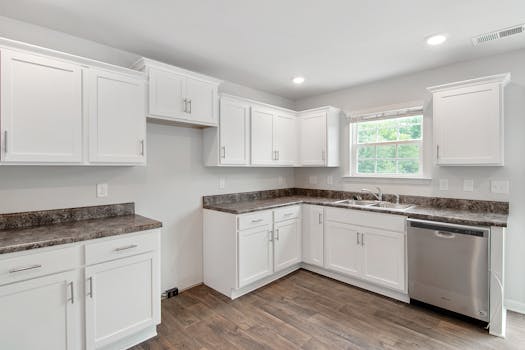 Spacious white kitchen featuring stainless steel appliances, white cabinets, and wood flooring.