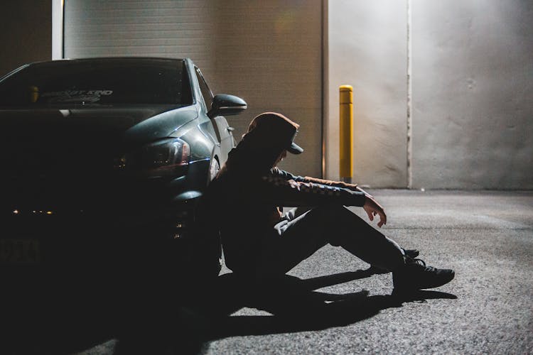 Anonymous Upset Young Guy Sitting On Ground Leaning On Car Tire