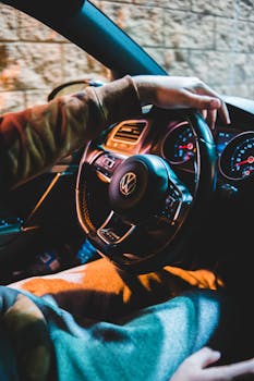 A man driving a car at night, focusing on the steering wheel and dashboard in a modern car interior.
