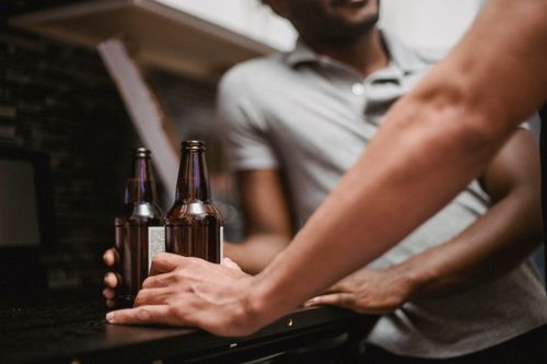 Free Two adults holding beer bottles in a relaxed indoor setting, fostering social interaction. Stock Photo
