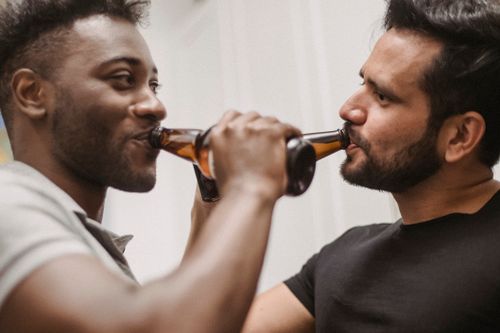 Free Two smiling men enjoying bottled beers while socializing indoors. Stock Photo
