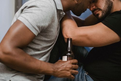 Free Two men embrace closely while sharing a beer, conveying love and connection. Stock Photo