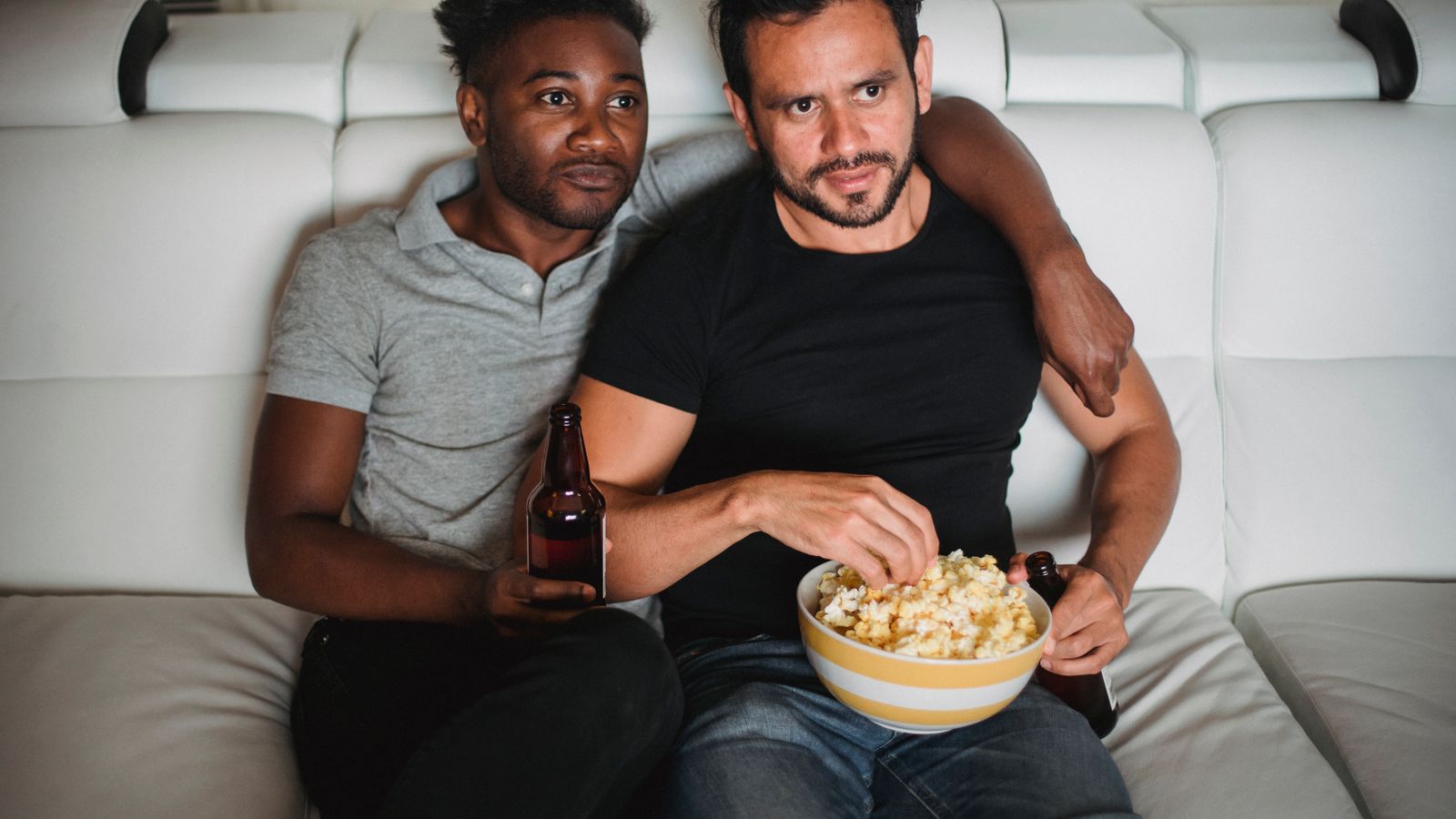 Two adults sharing popcorn on a sofa while watching a film