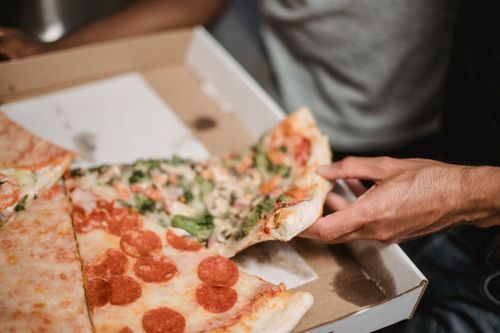 Free A close-up of a hand grabbing a slice from a pizza box with various toppings. Stock Photo