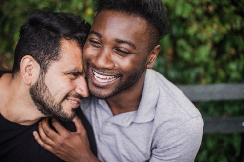 Free A loving LGBTQ couple smiling and embracing on a park bench, enjoying their time together. Stock Photo