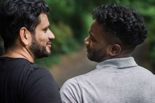 Free A close moment of affection between two men enjoying a walk in a lush, green outdoor setting. Stock Photo