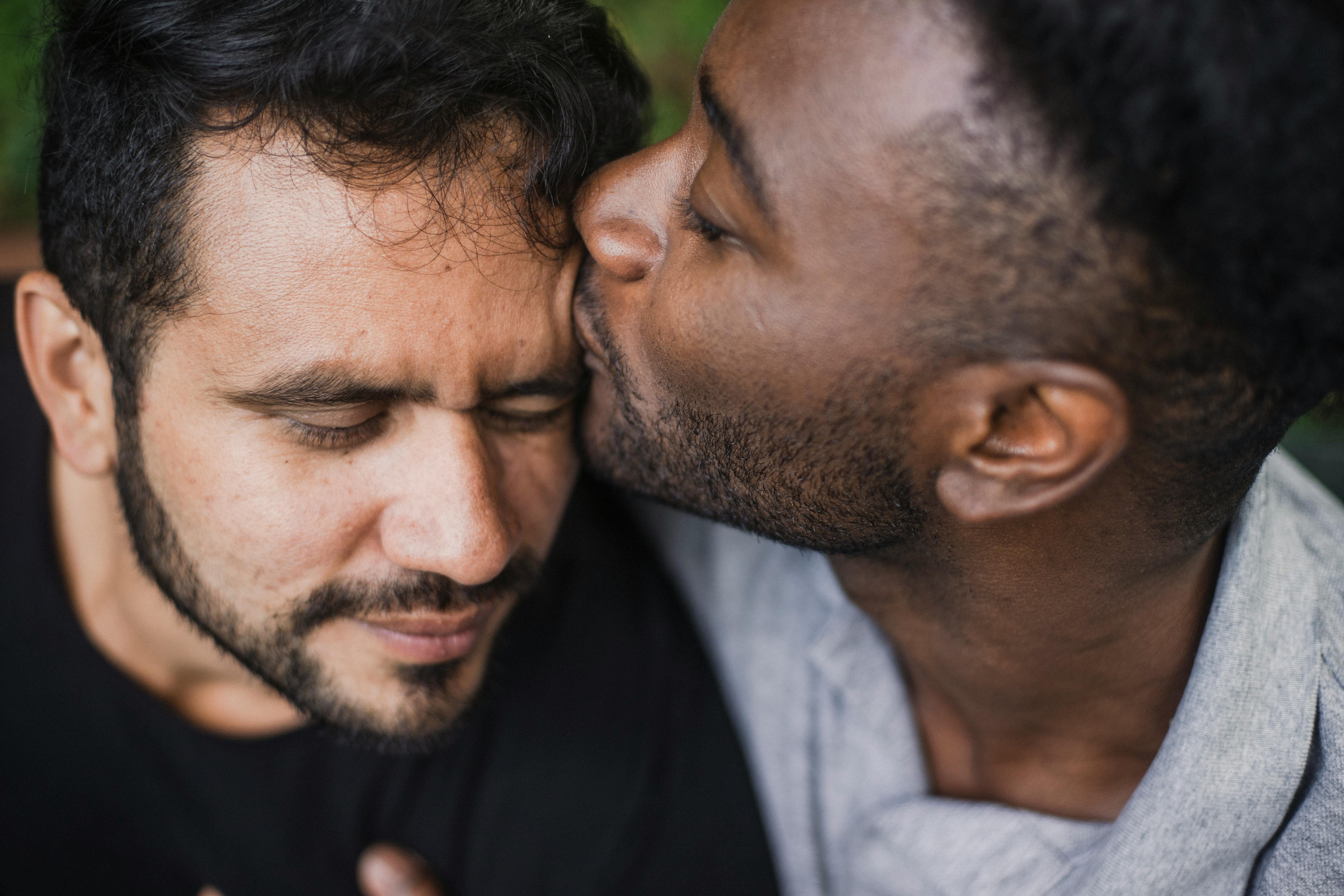 Close-up of two men, one kissing the other's forehead, showing love and affection.