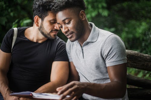 Photo of a Man in a Gray Shirt Reading a Book Beside a Man 