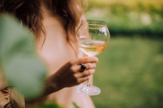 特写镜头捕捉到一位女士在户外手持一杯白葡萄酒，尽显轻松的夏日氛围