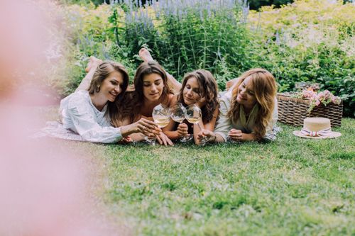 Free Four women relaxing in a garden, enjoying wine and togetherness. A perfect summer picnic scene. Stock Photo