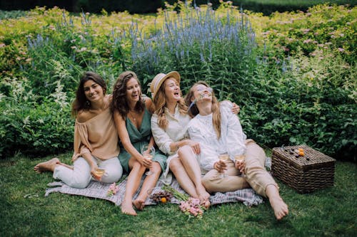 Happy Women Sitting Next to Each Other on a Picnic Blanket