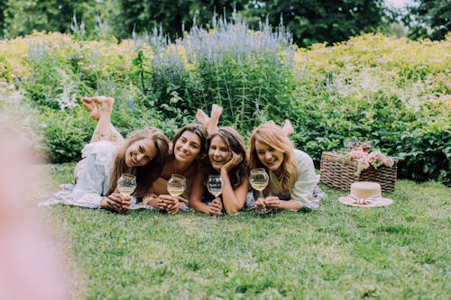 Photo of a Group of Women Lying on the Grass while Holding Their Drinks