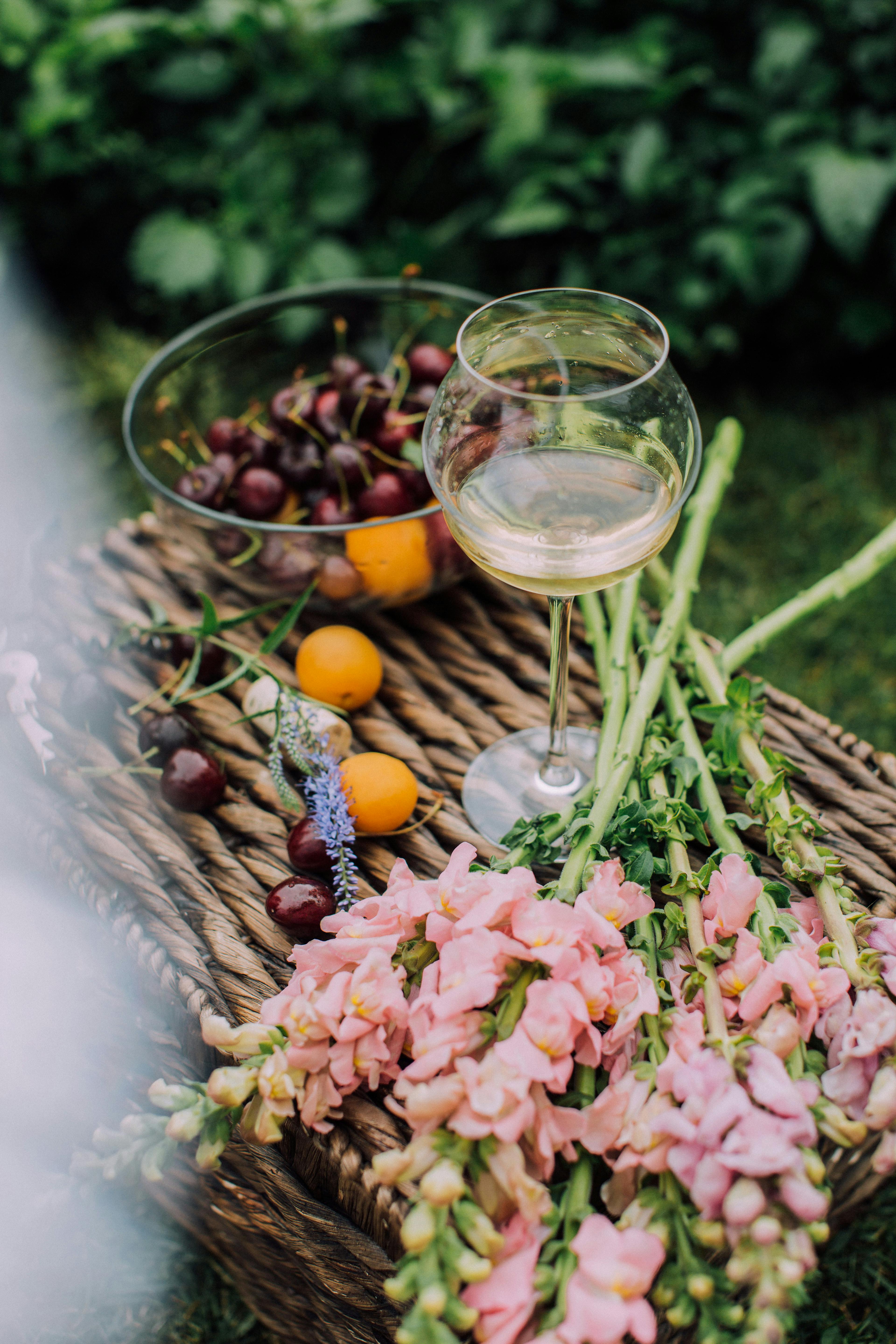 photo of a glass of wine and a bowl of fruits on top of a basket