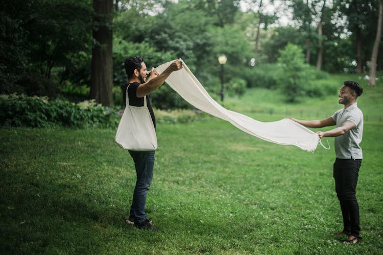 Men Laying Out The Blanket On The Grass Field